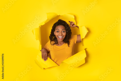 Joyful Black Lady Posing Looking Through Hole In Yellow Paper © Prostock-studio