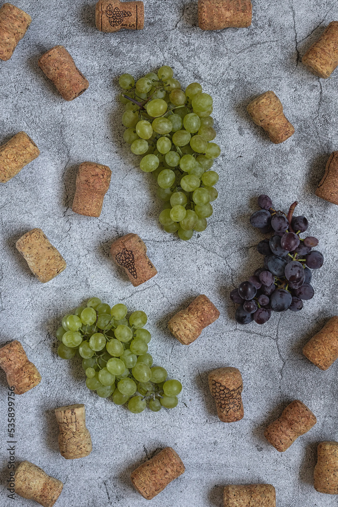 Pattern. Flat lay. Bunches of green and blue grapes and wine corks on a light gray background. Top view. 