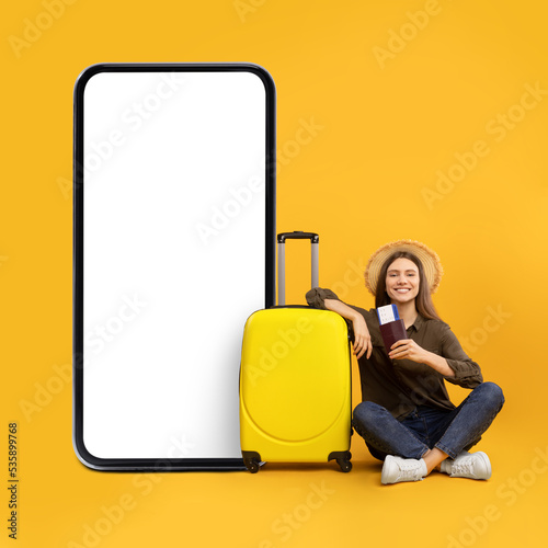 Female Sitting Near Large Smartphone With Blank Screen, Yellow Background