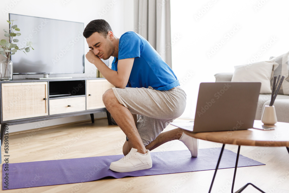 Fitness burnout. Exhausted arab man tired of online workout exercising at laptop sitting on fitness floor at home Fitness burnout. Exhausted arab man tired of online workout exercising at laptop sitting on fitness floor at home