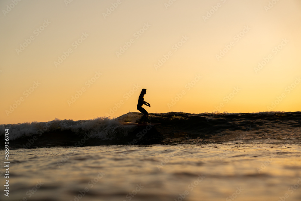 Surfista mujer en atardecer surf ola sobre tabla de surf cielo naranja