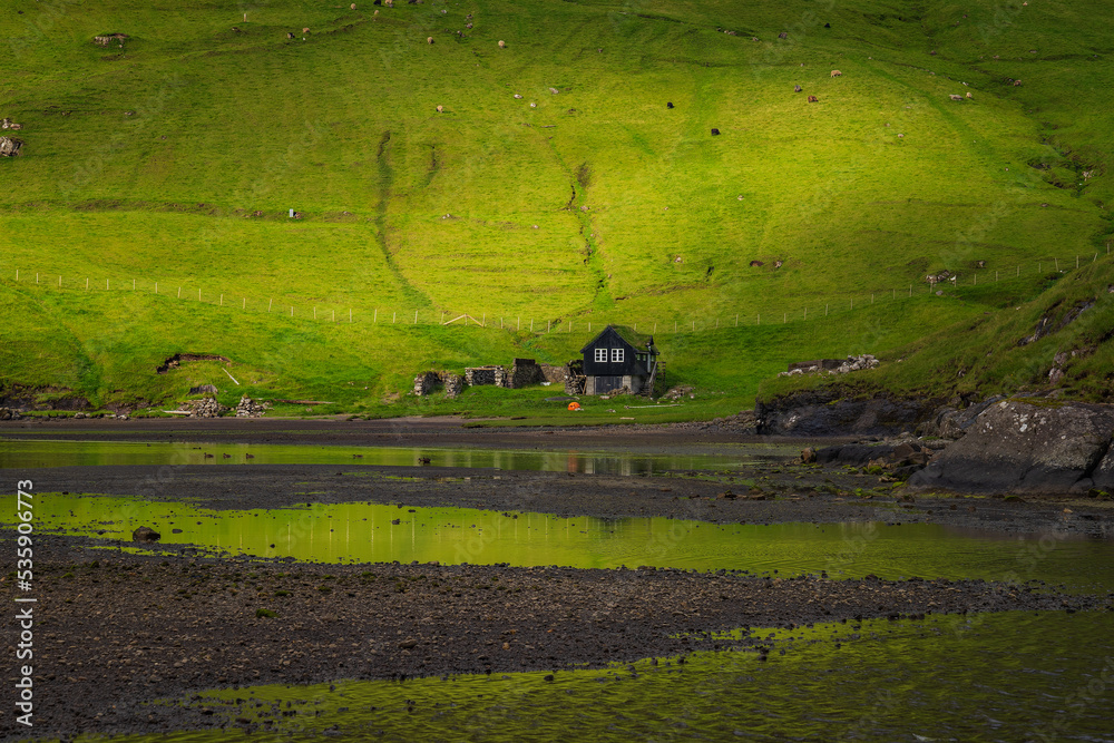Naklejka premium Saksun is a remote little village on Streymoy island in the wild Faroe Islands. The village is famous for its unique location placed above a jaw-dropping lagoon. 