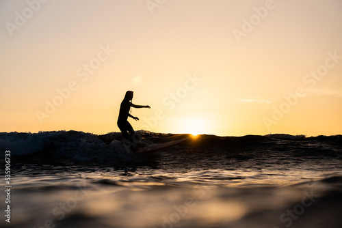 Surfista mujer en atardecer surf ola sobre tabla de surf cielo naranja