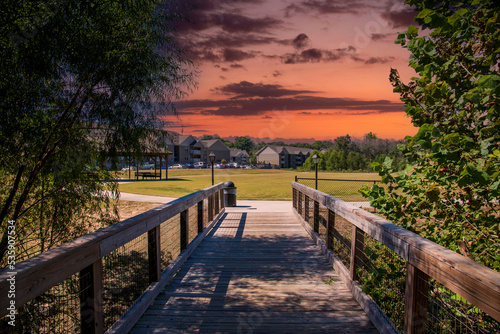 a long winding brown wooden bridge over the Sandy Run Creek surrounded by lush green trees and plants with powerful clouds at sunset at The Walk at Sandy Run in Warner Robins Georgia USA photo