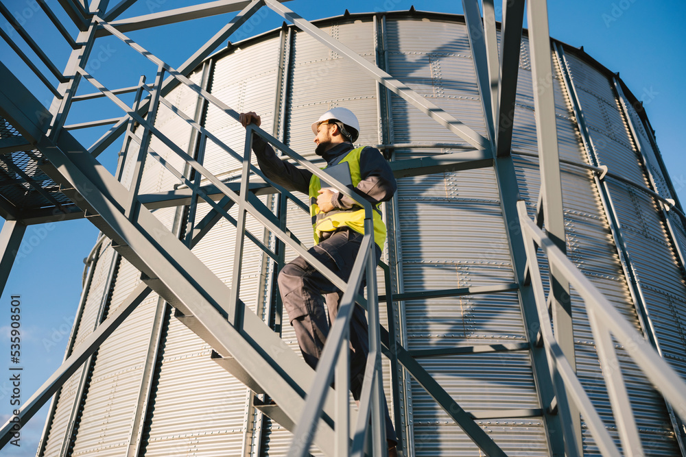 A supplies supervisor climbs up the stairs on a silo and checks supplies.