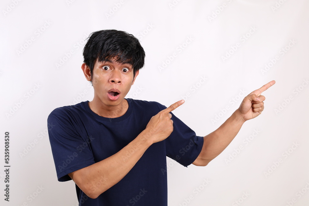 Surprised asian young man standing while pointing sideways. Isolated on white background with copyspace Surprised asian young man standing while pointing sideways. Isolated on white background with copyspace