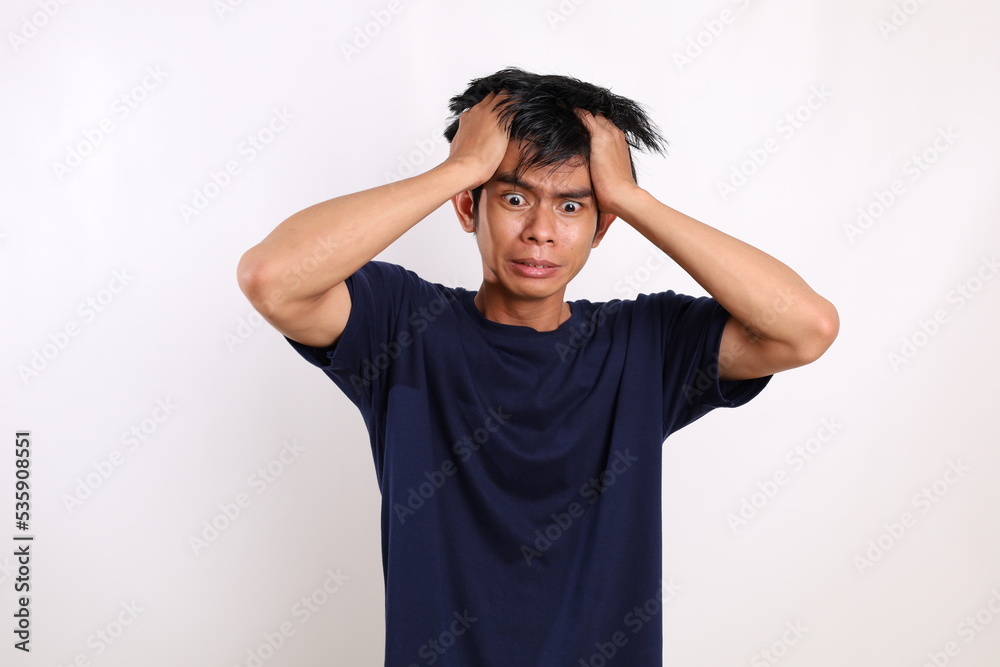 Frustrated asian young man standing while holding his head. Isolated on white background Frustrated asian young man standing while holding his head. Isolated on white background
