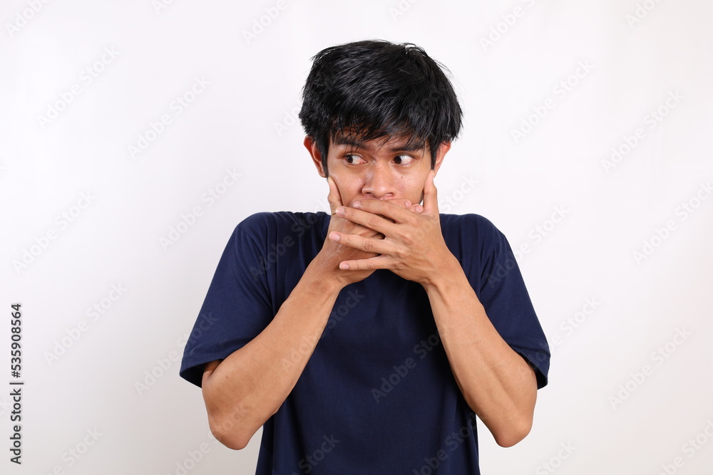 Asian young man covering his mouth while glancing sideways. Isolated on white background Asian young man covering his mouth while glancing sideways. Isolated on white background