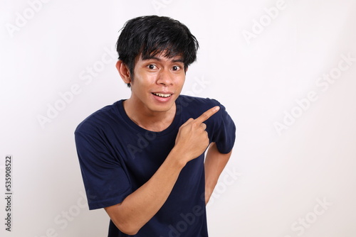 Happy asian young man standing while pointing sideways. Isolated on white background with copyspace