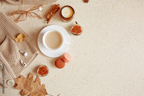 Fall lifestyle flat lay - casual sweater  woman glasess with headphones. Aesthetic coffee time among candle  fall leaves  macaroons cinnamon sticks. Copy space
