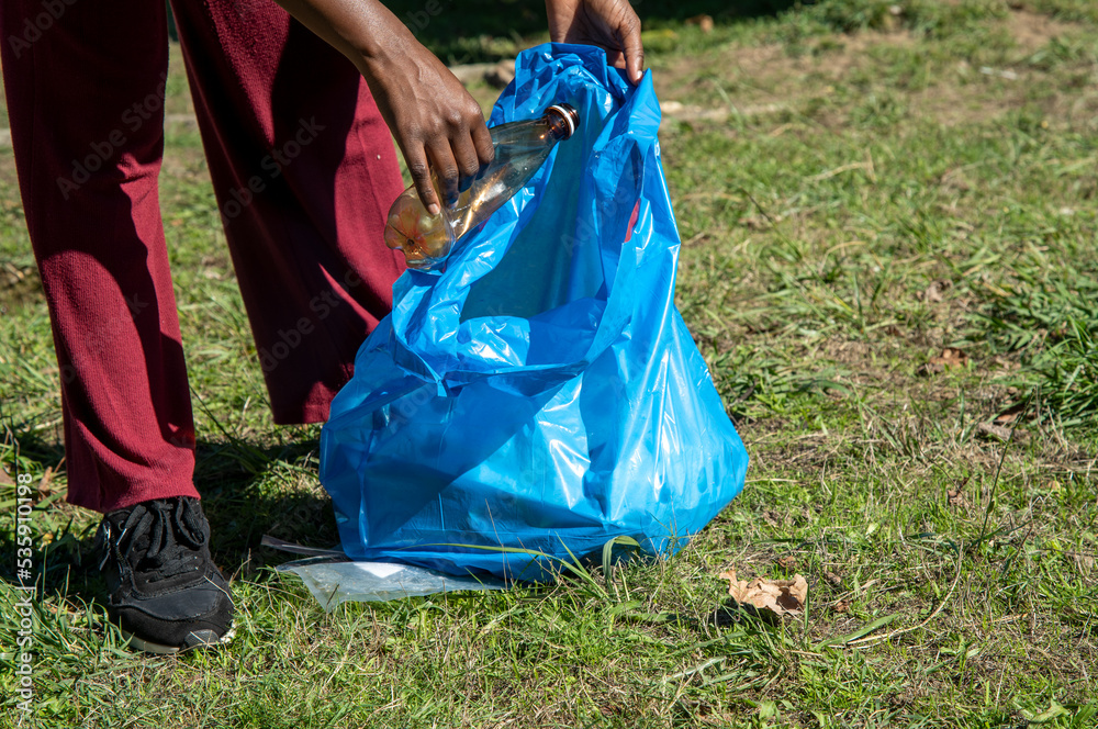 Young woman cleaning up plastics from field. Collecting garbage in a plastic bag Young woman cleaning up plastics from field. Collecting garbage in a plastic bag