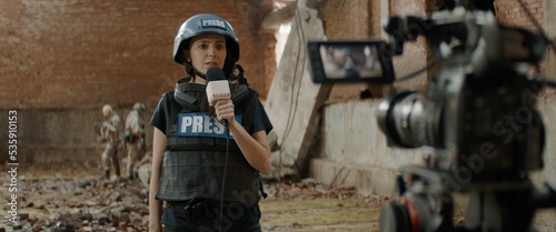 POV Camera view, female war journalist correspondent wearing bulletproof vest and helmet reporting live near destroyed building