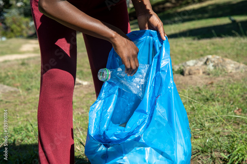 Young woman cleaning up plastics from field. Collecting garbage in a plastic bag