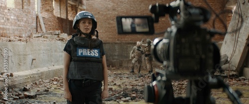 POV Camera view, female war journalist correspondent wearing bulletproof vest and helmet reporting live near destroyed building
