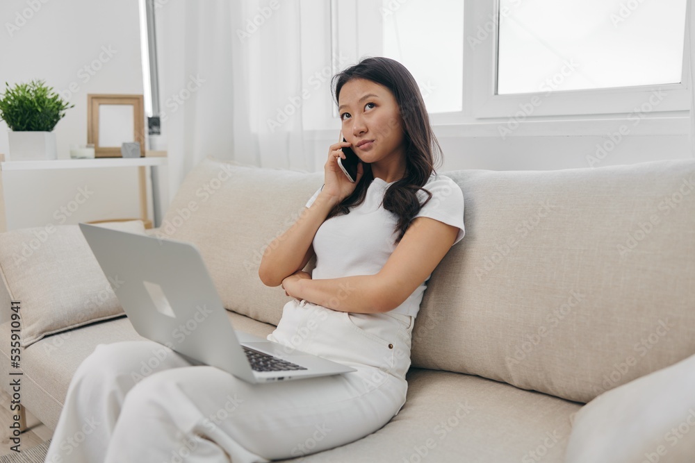 Asian Millennial woman sitting with laptop and talking on phone freelance student with looking at laptop screen working, lifestyle work and home Asian Millennial woman sitting with laptop and talking on phone freelance student with looking at laptop screen working, lifestyle work and home