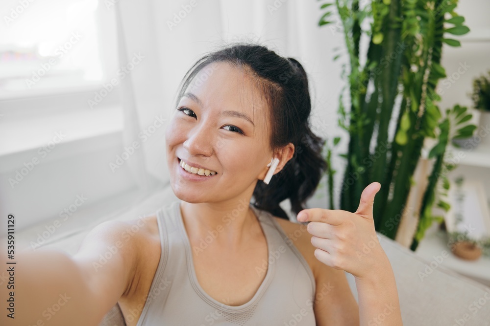 Athletic woman Asian blogger filming herself on camera and smiling with headphones waving, freelance work from home, recording athletic workouts lifestyle Athletic woman Asian blogger filming herself on camera and smiling with headphones waving, freelance work from home, recording athletic workouts lifestyle