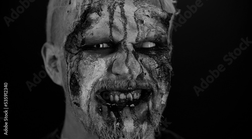 Close-up macro frightening man face with Halloween zombie blood flows and drips on face, trying to scare, smiles terribly with dirty teeth. Horror theme. Sinister undead guy. Serious body injury wound