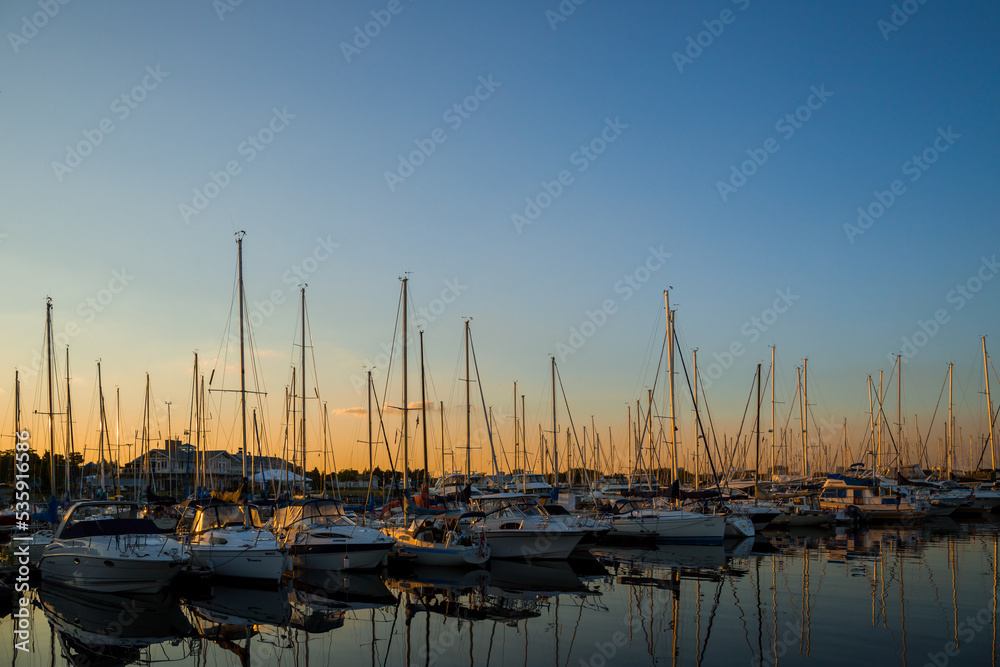 Small boats and yachts in a bay of lake at sunset light.