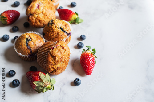 Blueberry and strawberry muffins with berries on a marble background. Close up and copy space.