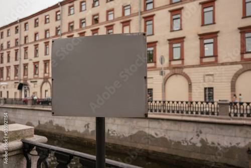Gray colored blank signage mounted on pole at city street against building background