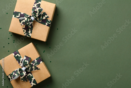 Fotografie Gift boxes with camouflage military ribbon bow on green table