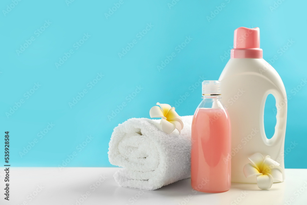 Bottles of laundry detergents, towel and plumeria flowers on white table. Space for text Bottles of laundry detergents, towel and plumeria flowers on white table. Space for text