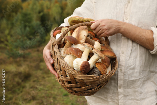 Man holding wicker basket with fresh wild mushrooms outdoors