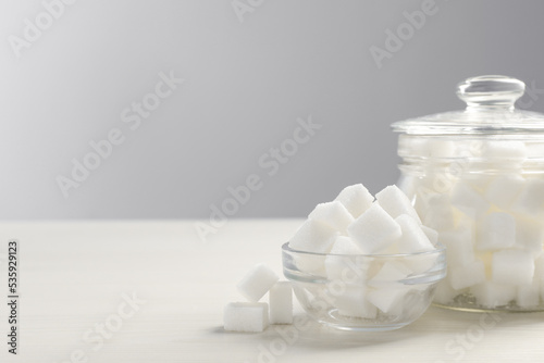 Glass jar and bowl with white sugar cubes on table, space for text