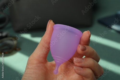 Woman holding violet menstrual cup on blurred background, closeup