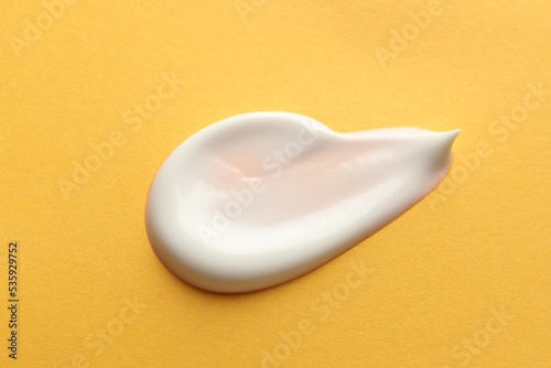 Sample of face cream on orange background, top view