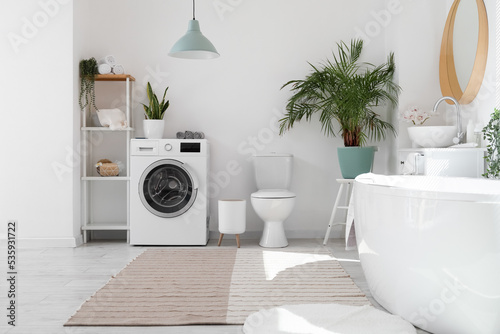 Stylish interior of bathroom with bathtub and washing machine