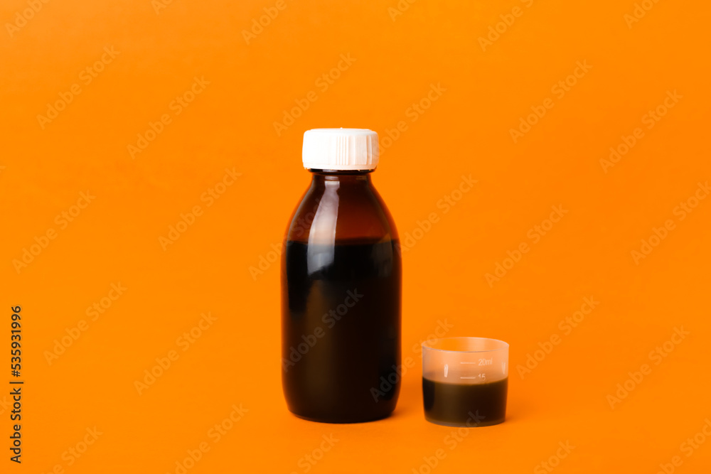 Bottle of cough syrup and cup on orange background Bottle of cough syrup and cup on orange background