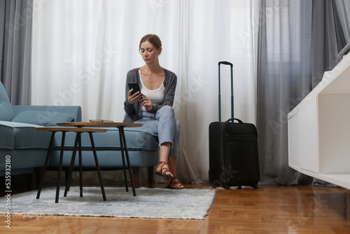 Young woman traveller with smartphone and luggage in hotel room