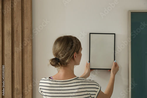 Woman arranging picture frames on wall in new house, diy home improvement concept 