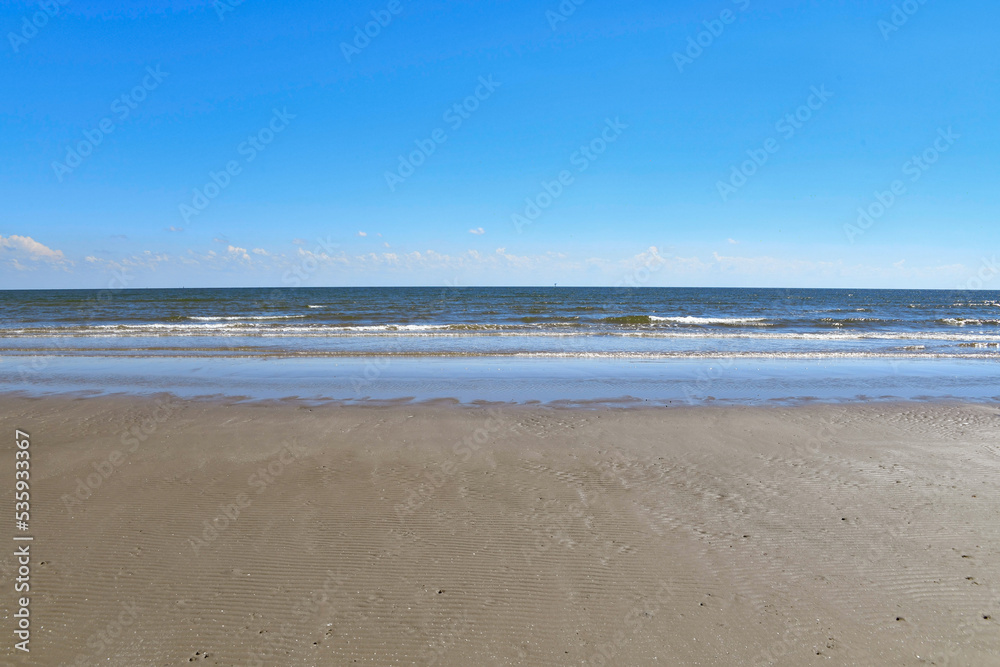 deserted empty beach with fluffy clouds on the horizon and clear blue sky
