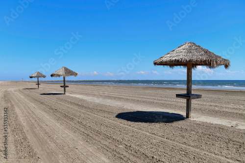 Canvastavla palapas on a deserted, empty beach with surf and a jetty in the distance