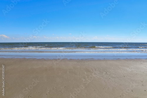 deserted empty beach with fluffy clouds on the horizon and clear blue sky