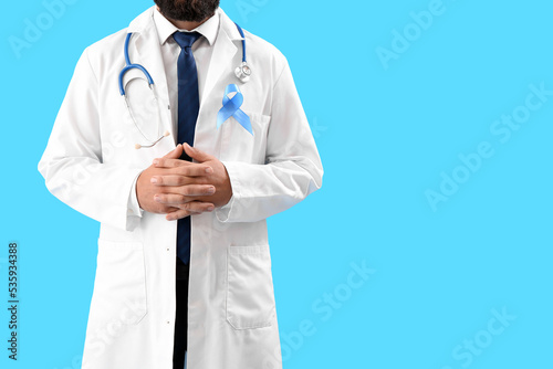 Male urologist with blue awareness ribbon on color background. Prostate cancer concept