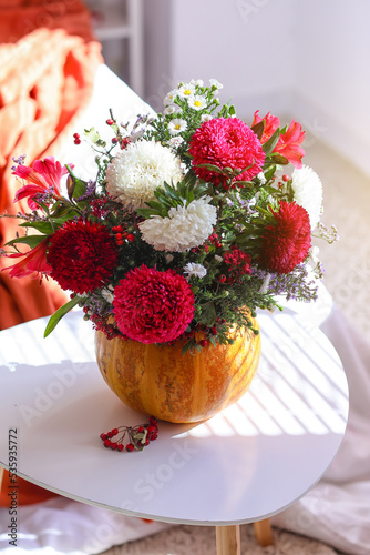 Pumpkin with autumn flowers on table in light bedroom, closeup