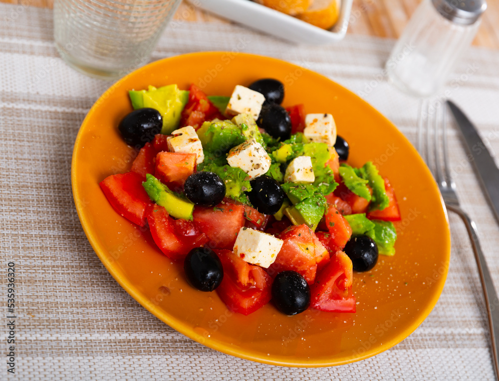 Portion of fresh avocado salad with feta cheese, tomatoes and black olives.