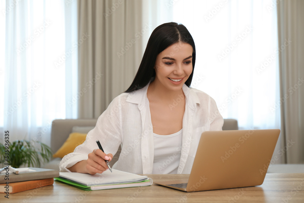 Young woman taking notes during online webinar at table indoors Young woman taking notes during online webinar at table indoors