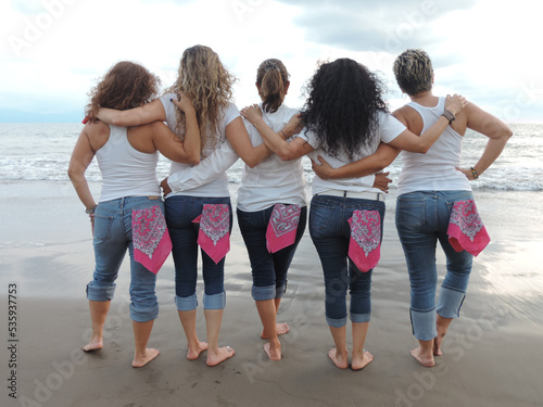 Fototapeta Naklejka Na Ścianę i Meble -  women hugging back to back in denim jeans and pink bandanas on the beach, pinktober