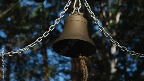 Big copper and bronze bell hanging on chains outdoor. Ringing metal bell close up. photo