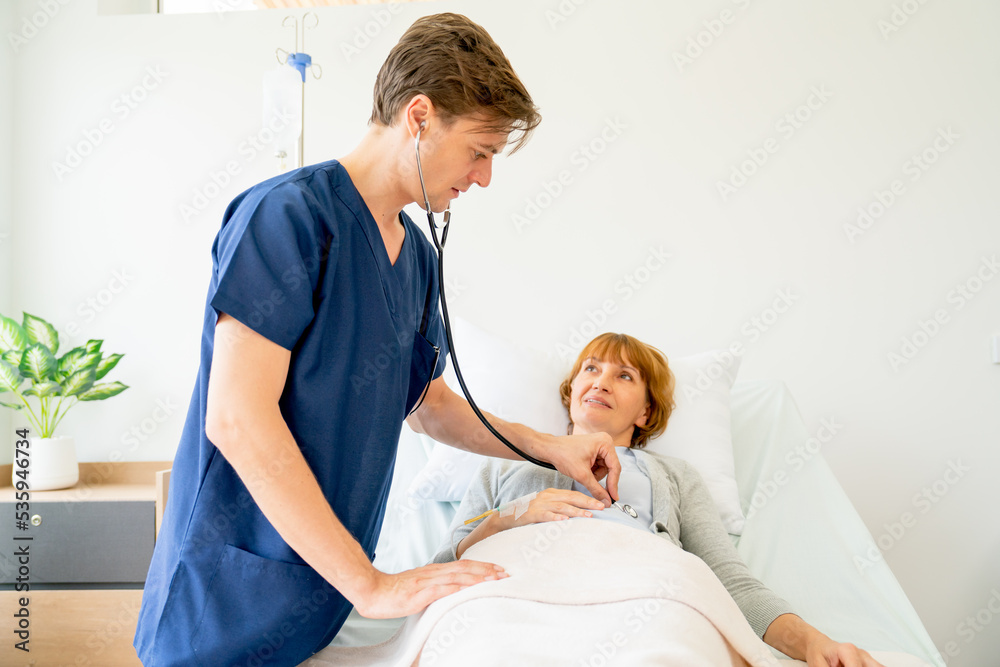 Fototapeta premium Young Caucasian doctor use stethoscope to check or diagnosis the symptom of senior patient who lie on bed in patient room.