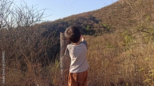 niño señalando los cerros parado junto a un alambrado