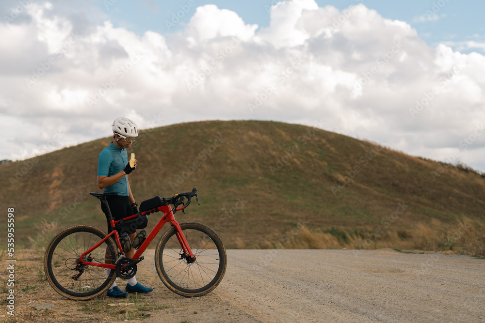 Cyclists practicing on gravel roads. he is eating a banana