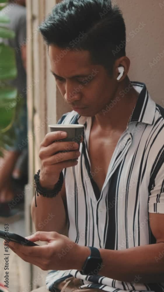 VERTICAL VIDEO: Young man sits outside and uses mobile phone VERTICAL VIDEO: Young man sits outside and uses mobile phone