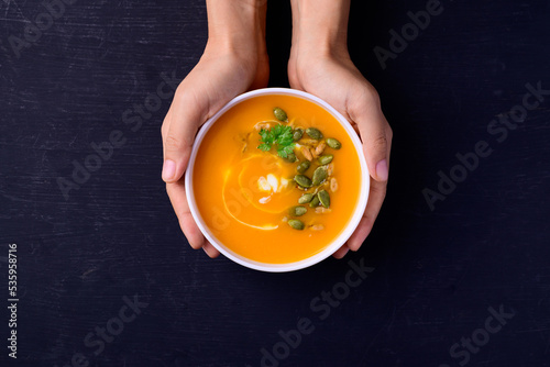 Obraz na plátně Butternut squash pumpkin soup in bowl holding by hand on black background, Homem