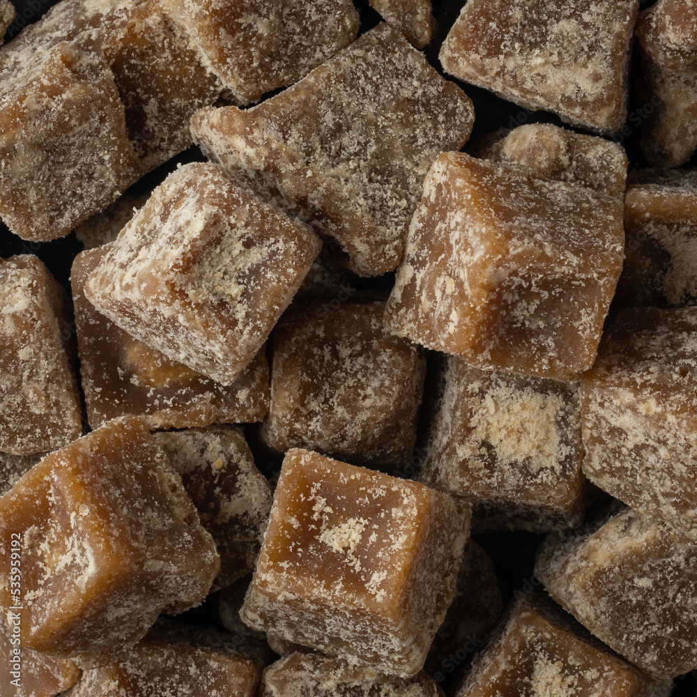 pile of jaggery pieces, golden brown colored cube shaped unrefined sugar product also called kithul jaggery or palm sugar, full frame background taken from above pile of jaggery pieces, golden brown colored cube shaped unrefined sugar product also called kithul jaggery or palm sugar, full frame background taken from above