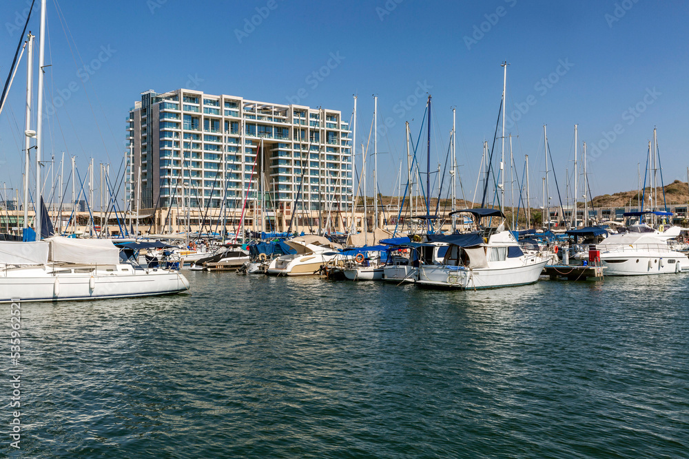 Marina with large yachts and wooden boats in the southern port city on a sunny bright day. Hotel building on the beach, beautiful scenery.